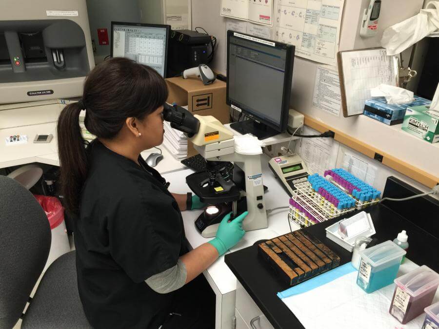 Woman in black scrubs looking through a microscope