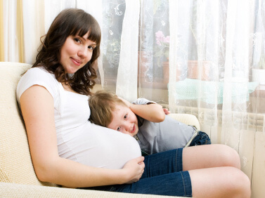 Youthful, pregnant mother sitting in a chair hugging her young son